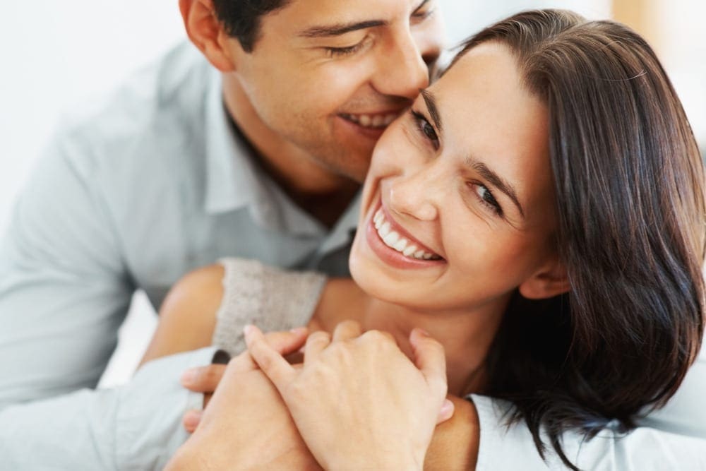Man and woman embracing as woman smiles at the camera.