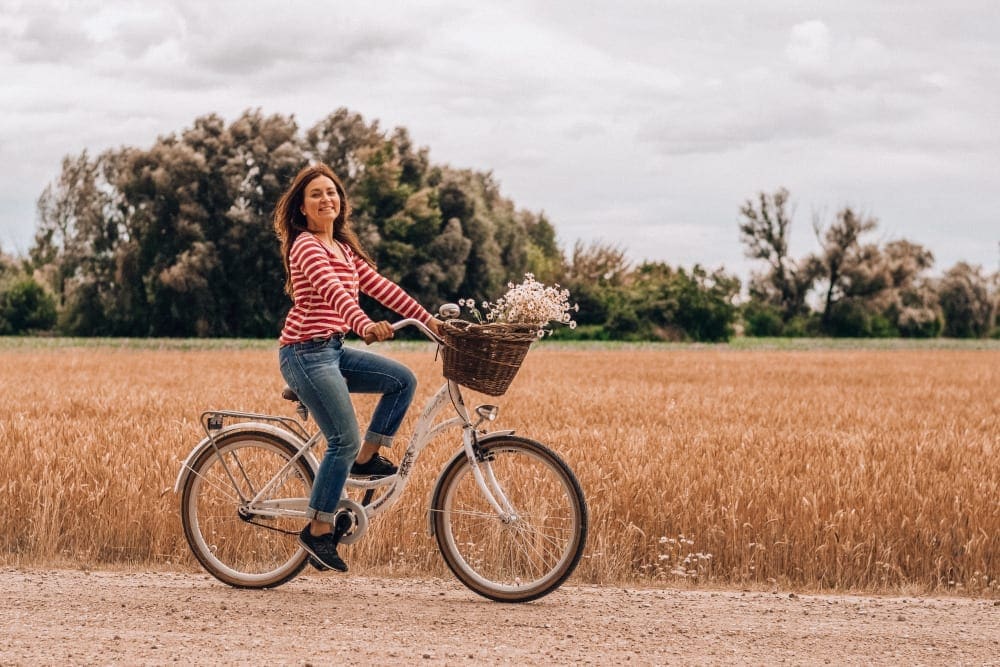 Woman riding a beach cruiser bike on a gravel road near a wheat field.