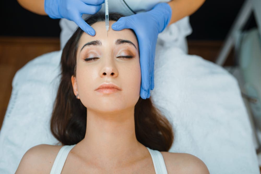 Woman getting face botox injections from medical professional wearing gloves.